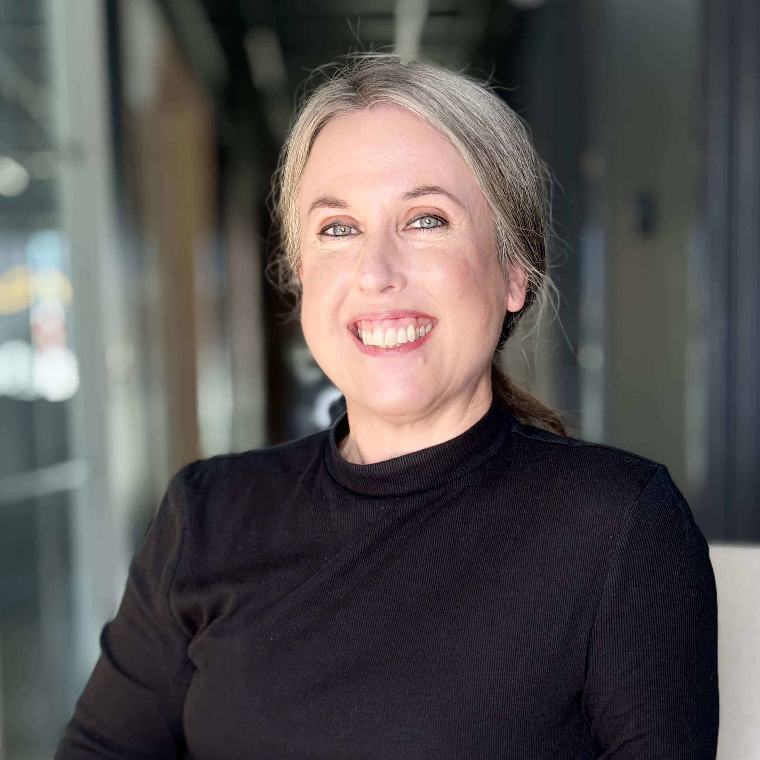 Close up of woman in black turtle neck smiling with hair pulled back.